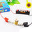 Small light bulb with wires and clips on a white background, with a battery and colorful packaging in the background.