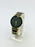 Watch with black and gold band on a white stand