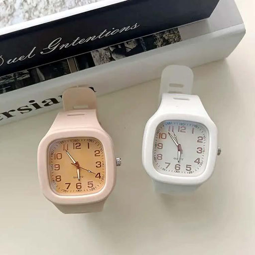Two wristwatches, one pink and one white, on a surface with a magazine in the background.
