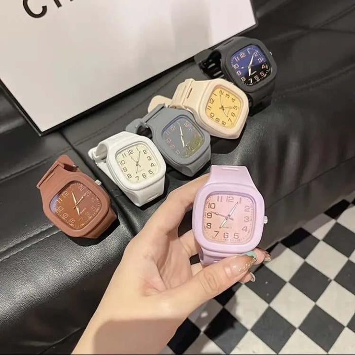 Hand holding a pink watch with other colorful watches on a checkered floor.