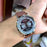 Wrist wearing a Curren watch with a brown leather strap.