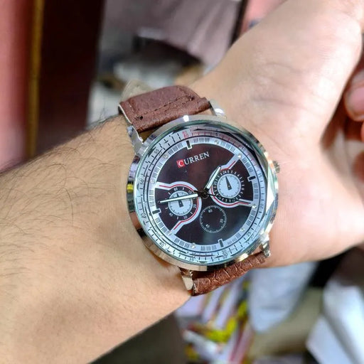 Wrist wearing a Curren watch with a brown leather strap.