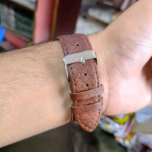 Brown leather watch strap on a wrist with a blurred background