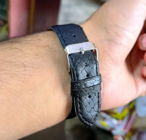Black leather watch strap on a wrist with a blurred background