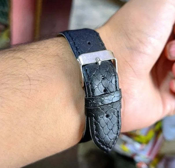 Black leather watch strap on a wrist with a blurred background