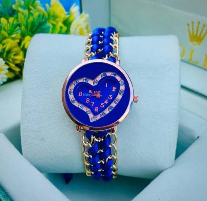 Blue heart-shaped watch with gold accents on a white cushion, with a blurred background