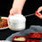 Person using a small white container with a spoon, surrounded by food on a dark surface.