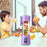 Two people drinking orange juice from a purple portable blender filled with fruits in a kitchen setting.