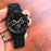 Black wristwatch held in a hand on a wooden surface