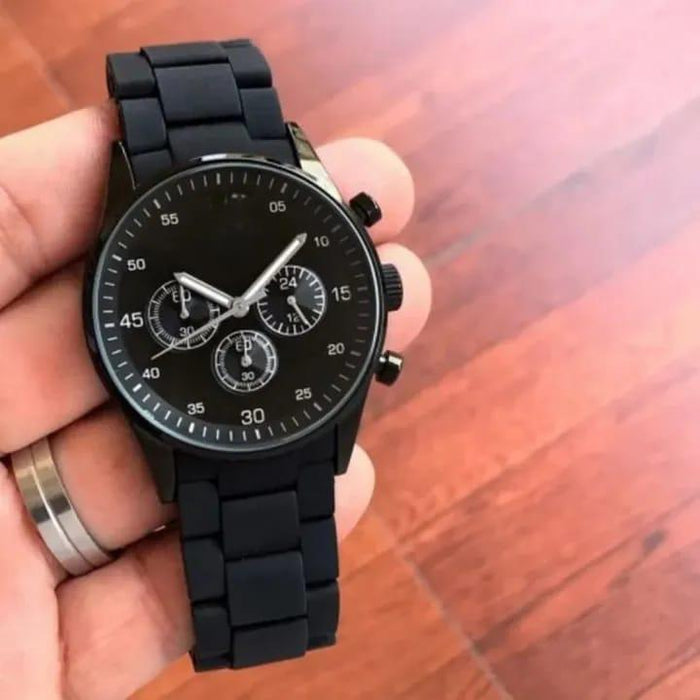 Black wristwatch held in a hand on a wooden surface