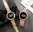 Two gold digital watches with diamond-studded straps on a gray surface.