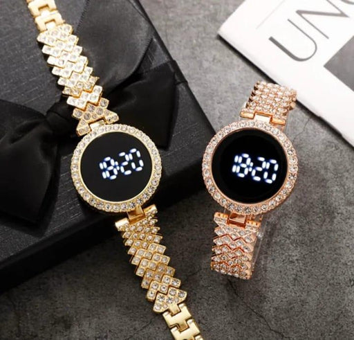 Two gold digital watches with diamond-studded straps on a gray surface.