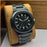 Black wristwatch with metal strap on a brown cushion against a wooden background