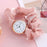 Small round watch with gold rim on a pink fabric background