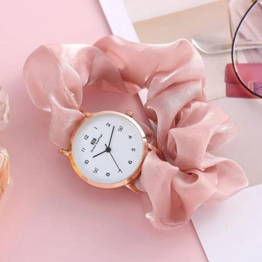 Small round watch with gold rim on a pink fabric background
