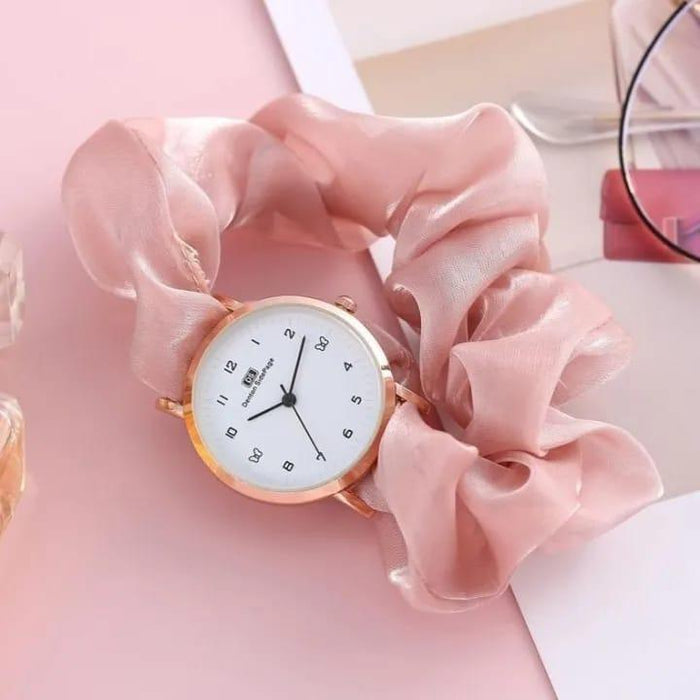 Small round watch with gold rim on a pink fabric background