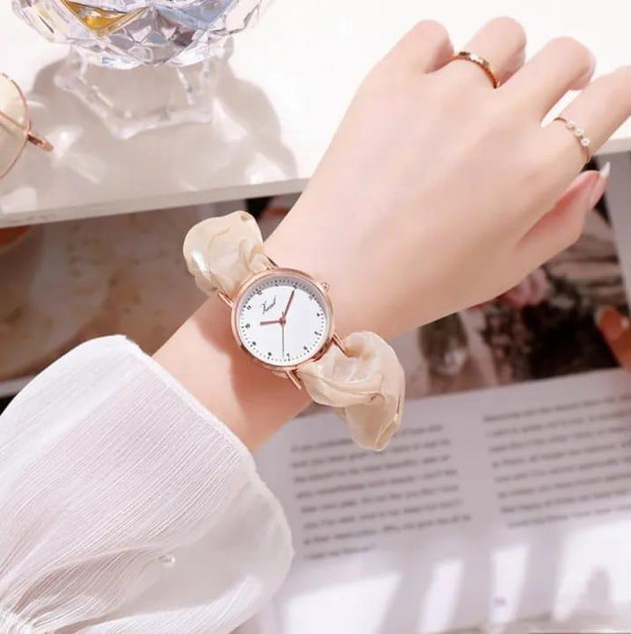 Hand wearing a watch with a marble-like strap on a blurred background