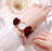 Hand wearing a watch with a red bow on a light background