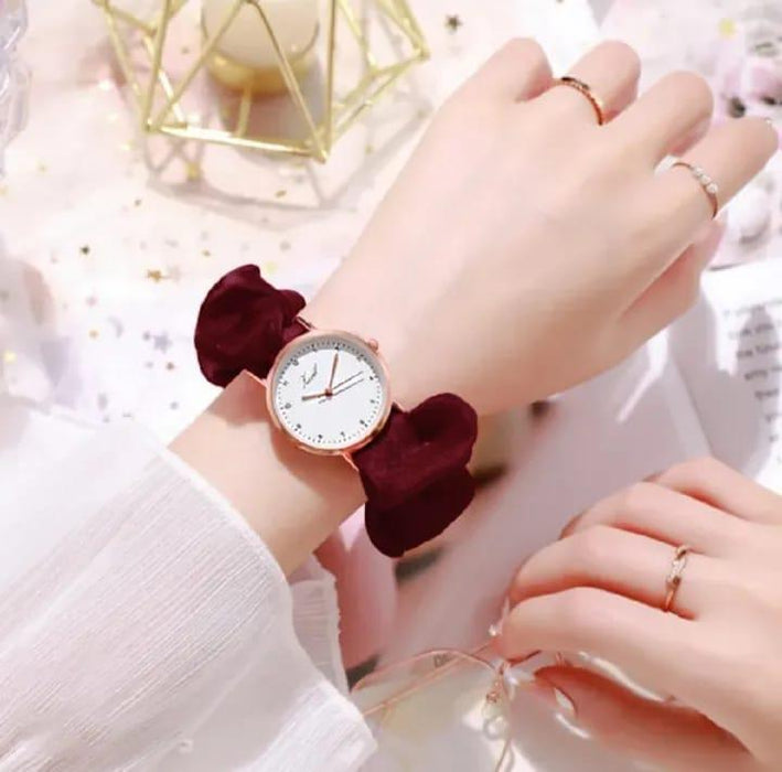Hand wearing a watch with a red bow on a light background