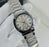 Silver watch with a white face featuring Roman numerals on a white surface.