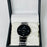 Black wristwatch with silver band in a black box on a white background