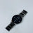Black wristwatch with a silver band on a light gray background