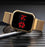 Gold digital watch with red display on a dark surface